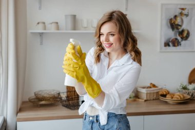 A girl in yellow gloves holds a cleaning spray on the background of the kitchen. High quality photo
