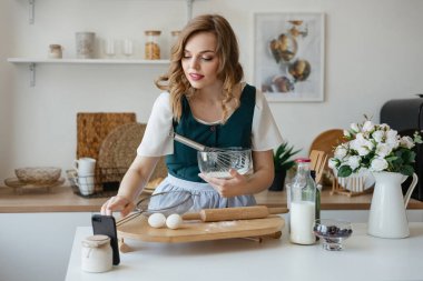 Beautiful girl cooks and looks at the recipe on the smartphone. High quality photo