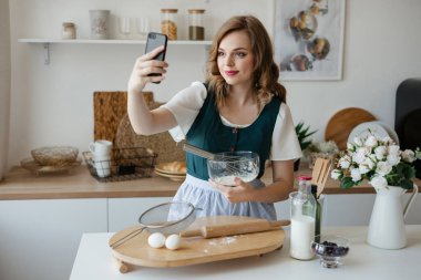Beautiful girl cooks and looks at the recipe on the smartphone. High quality photo