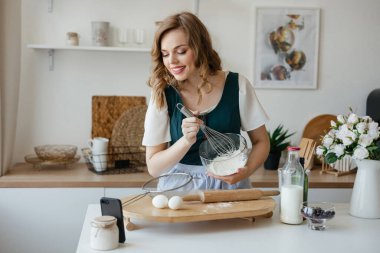 Beautiful girl cooks and looks at the recipe on the smartphone. High quality photo