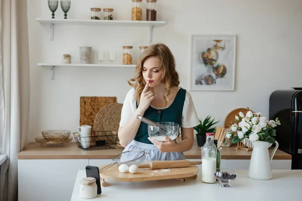 Beautiful girl cooks and looks at the recipe on the smartphone. High quality photo
