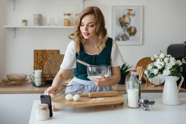 Beautiful girl cooks and looks at the recipe on the smartphone. High quality photo