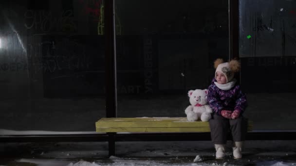 Flicka sitter ensam på natten vid busshållplatsen — Stockvideo