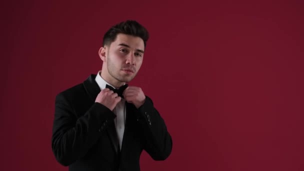 Snygg man på en röd bakgrund justerar sin kostym och flörtar — Stockvideo