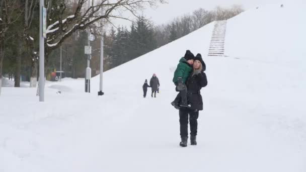 Мама берет сына на руки в снежном парке — стоковое видео