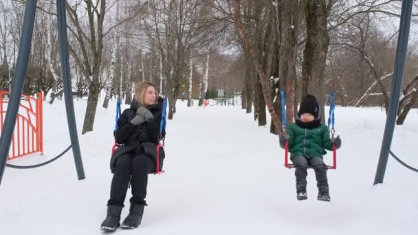冬の公園でスイングに乗ってお母さんと息子 — ストック動画
