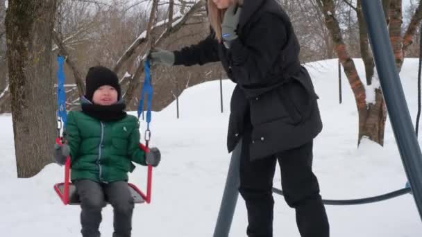 Mamá entretiene al bebé en un columpio de invierno — Vídeos de Stock