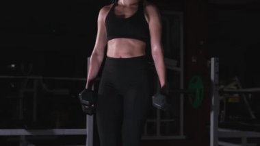 Sarışın, kalça kaslarını ve kollarını sallıyor. Ağırlıklı hamleler. Güzel bir atletik figür. İnce mide. Güçlü bacaklar.