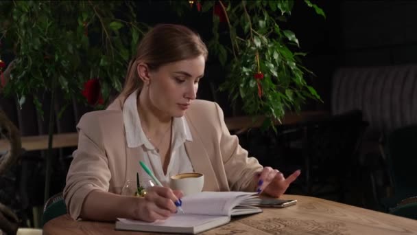 一个漂亮的金发姑娘喝咖啡，然后在笔记本上写字 — 图库视频影像