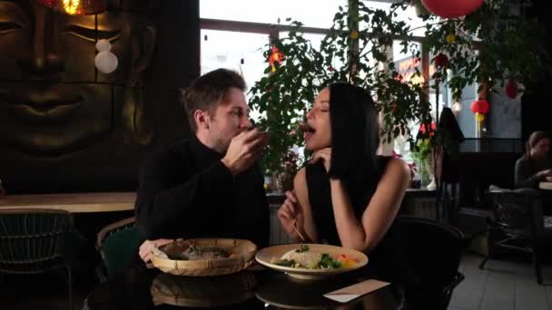 Mężczyzna karmi dziewczynę pałeczkami, a potem chciwie ją całuje. — Wideo stockowe