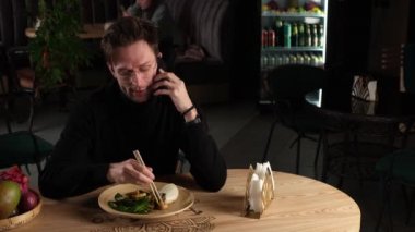 Siyah balıkçı yakalı bir adam kafede telefonla konuşuyor.