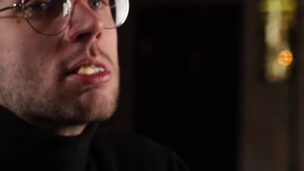 En kille med glasögon äter aptitligt en bulle — Stockvideo