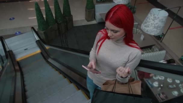 Дівчина їде на ескалаторі і дивиться на телефон — стокове відео