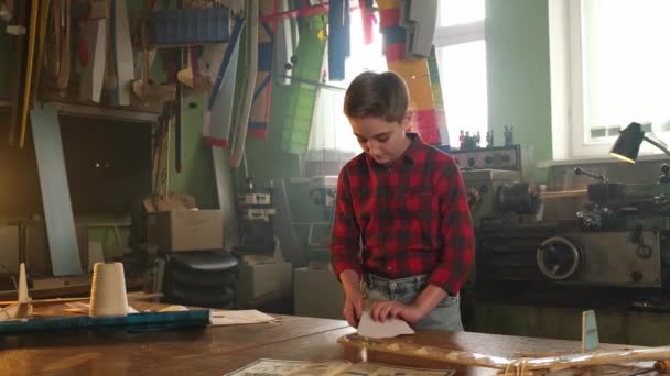 Een jongen in een geruit shirt maakt een papieren vliegtuig — Stockvideo