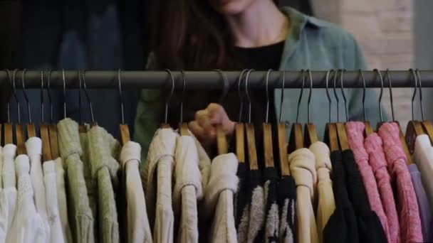 Το κορίτσι περνά μέσα από τις κρεμάστρες με γυναικεία ρούχα — Αρχείο Βίντεο