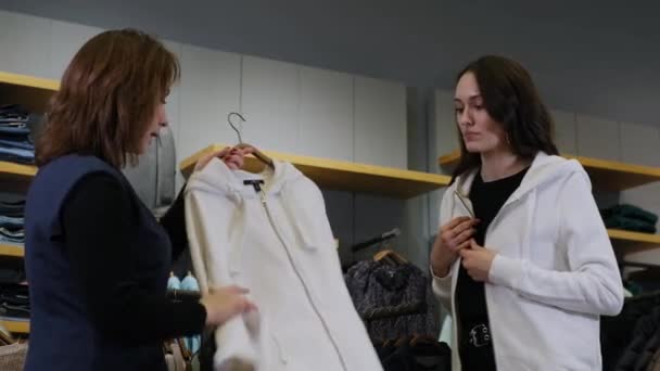 El asistente de ventas ayuda a la chica con la elección de la ropa — Vídeos de Stock