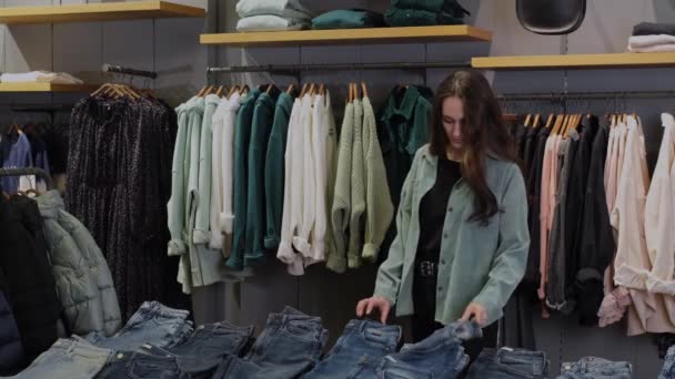 Продавец помогает девушке выбрать джинсы — стоковое видео