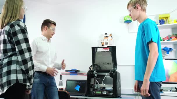 Młody nauczyciel wyjaśnia uczniom, jak działa drukarka 3D — Wideo stockowe