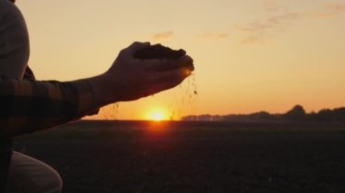 Bir tarımcı tarlada elindeki toprağı inceliyor. Ellerinizi yakın tutun.
