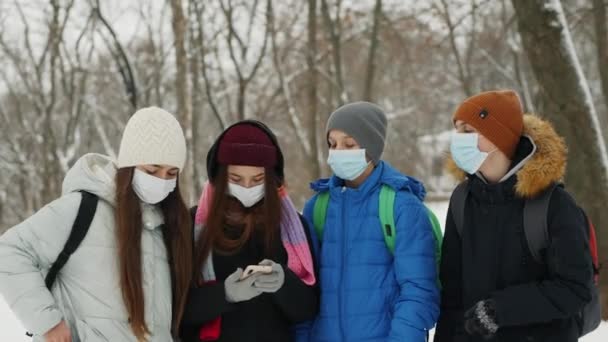 Група підлітків у медичних масках, що ходять разом у парку взимку — стокове відео