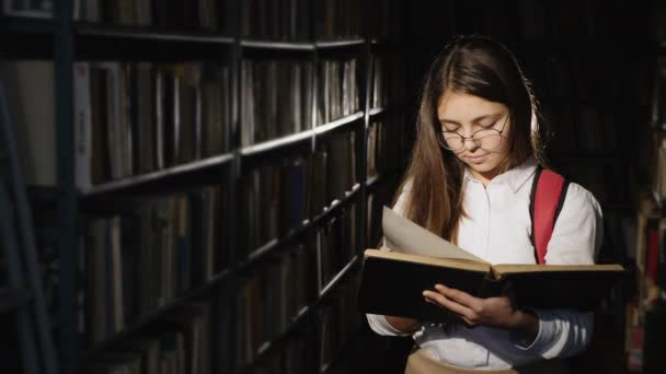 Estudante atenciosa lê um livro em pé na biblioteca — Vídeo de Stock