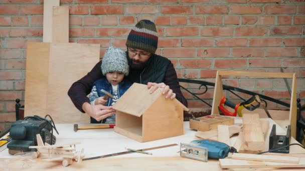 Папа и его маленький сын строят вместе кормушку для птиц — стоковое видео