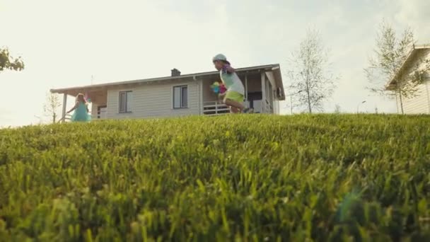 Счастливые маленькие дети бегают по зеленой лужайке и держат цветную игрушку ветряной мельницы — стоковое видео