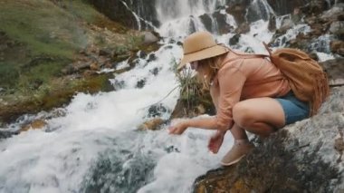 Bir turist bir dağ nehrinden su alır ve içer.