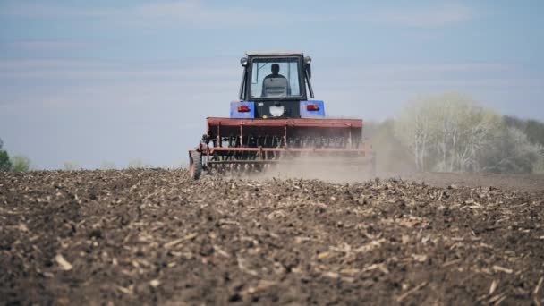 Vista trasera de un agricultor sobre un tractor sembrando granos de maíz en un campo agrícola seco — Vídeo de stock