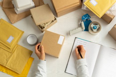 İş yerindeki depo işçisi teslimatları kutulara ve paketlere dağıtıyor, günlük tutuyor..