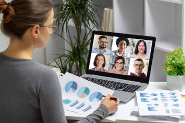 Bilgisayar kullanarak internet üzerinden iş adamlarıyla video konferansı. Bir kadın meslektaşlarıyla uzaktan konuşurken istatistiksel ve mali raporlar tutar.