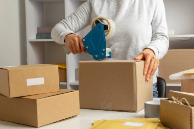 A warehouse worker seals a box with goods for delivery by mail with a dispenser.