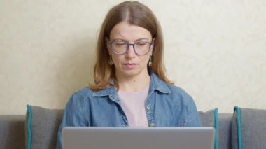 Genç bir kadın kanepede otururken uzaktan bilgisayarla çalışıyor..