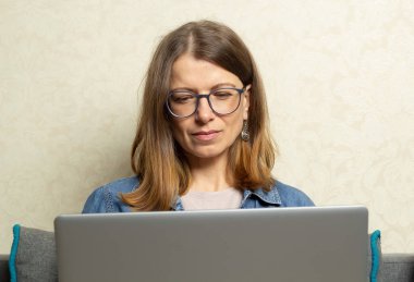 Genç bir kadın evdeki kanepede otururken dizüstü bilgisayarda çalışıyor..