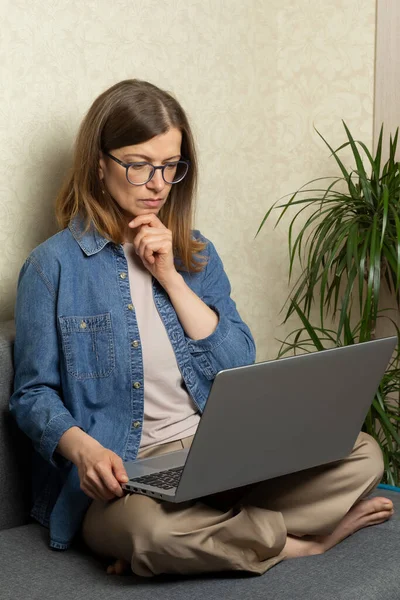 Genç bir kadın evdeki kanepede otururken dizüstü bilgisayarda çalışıyor..