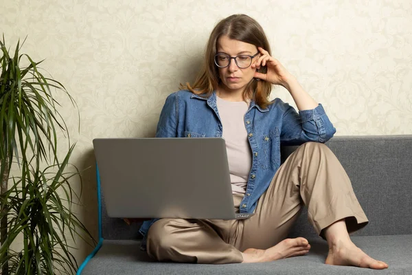 Genç bir kadın evdeki kanepede otururken dizüstü bilgisayarda çalışıyor..