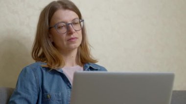Gözlüklü genç bir kadın dizüstü bilgisayarda çalışıyor..
