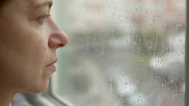 Sad Thoughtful Woman Stands Window Looks Raindrops Flowing Window Glass — Stockvideo