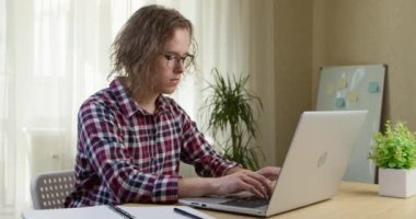 Genç bir adam iç mekanda otururken bir bilgisayar üzerinde çalışır. Bir öğrenci çevrimiçi eğitim için dizüstü bilgisayar kullanır.