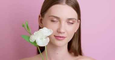 Flower touch of a beautiful girl's face with natural make-up and clear skin. Close-up of a young woman on a pink background. The concept of organic cosmetics.