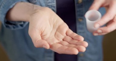 Bir kadın eline konteynırdan iki hap döküyor. Kapsül şeklinde ilaçlar alıyor..