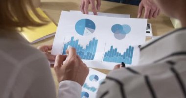 İş çizelgeleri, istatistikler, finansal analistlerin elinde. Masaüstündeki raporlarla çalışan bir grup insan.