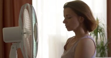 A woman is cooled by an electric fan in the heat in the room.