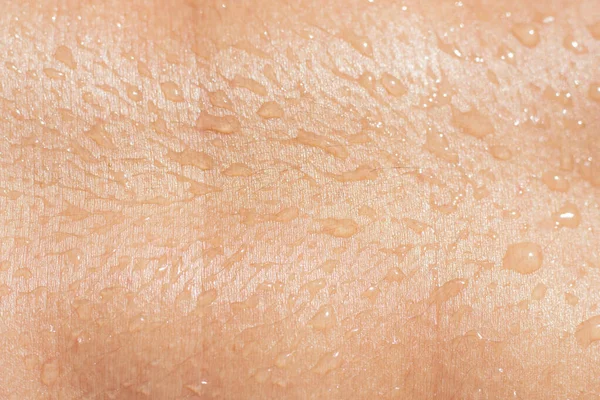Textura da pele feminina molhada com gotas líquidas close-up. corpo humano bronzeado com gotas de água. Imagens Royalty-Free