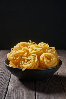 Ahşap masada çiğ makarnalı derin kase. Koyu arkaplanda çiğ makarna