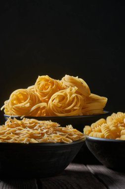 Üç derin kase ve ahşap bir masada pişmemiş makarna. Çiğ makarna çeşitleri.