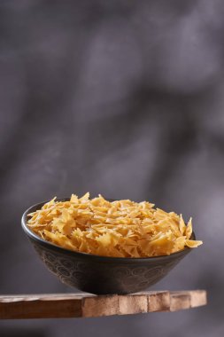 Ahşap masada çiğ makarnalı derin kase. Koyu arkaplanda çiğ makarna