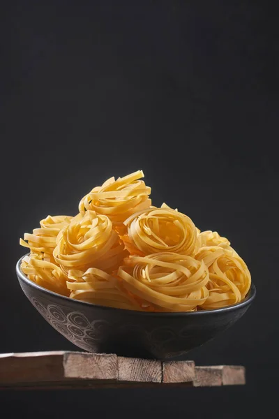 Deep bowl with raw pasta on wooden table. Raw pasta on a dark background