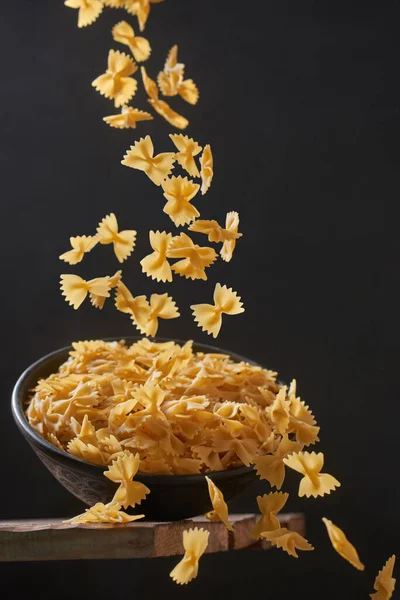 Deep bowl with raw pasta on wooden table. Raw pasta on a dark background. Falling paste, levitation effect