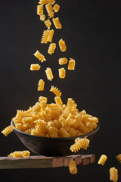 Deep bowl with raw pasta on wooden table. Raw pasta on a dark background. Falling paste, levitation effect